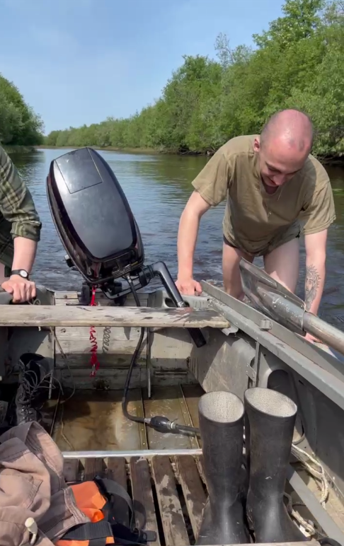 A team member at the outboard motor in a shallow channel