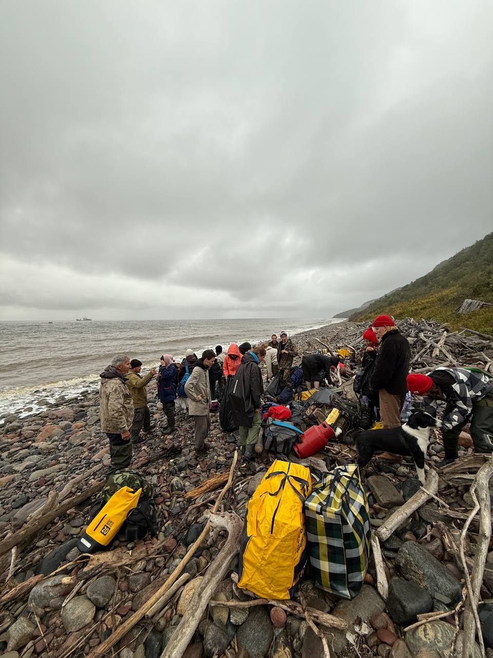 The team with backpacks on the rocky shore, waiting for the boat